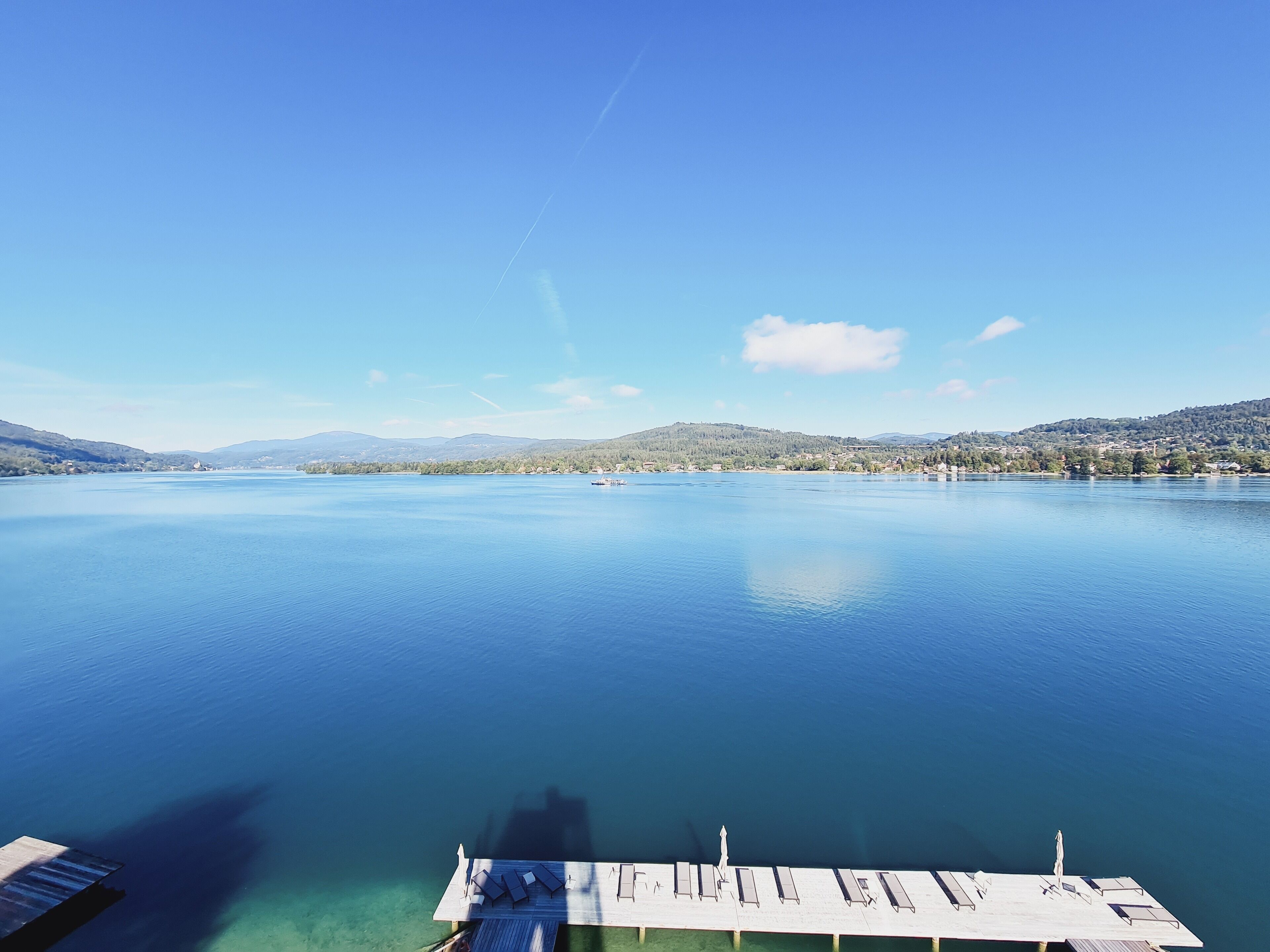 A calm lake with a wooden dock and lounge chairs.