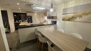 A modern kitchen with a central island, white cabinetry, and a dining area with a wooden table and chairs.