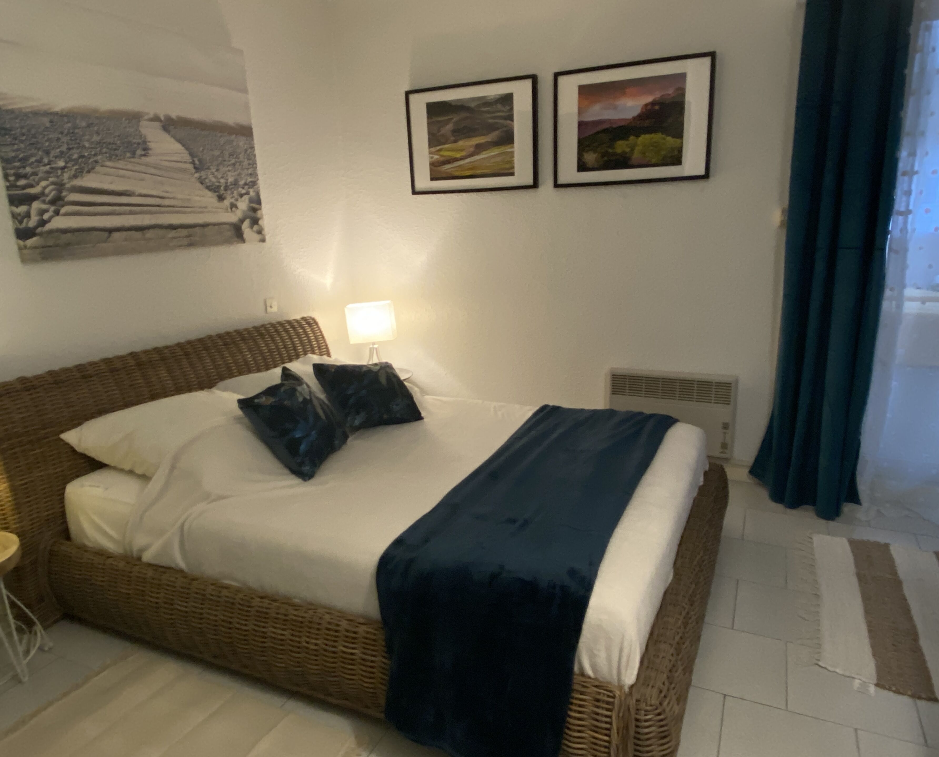 Ein Schlafzimmer mit Bett, Kissen, einer Nachttischlampe, einer Wand-Klimaanlage und zwei gerahmten Bildern.