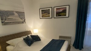 A bedroom with a bed, pillows, a bedside lamp, a wall-mounted air conditioner, and two framed pictures.