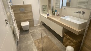 A modern bathroom with a glass shower enclosure, a white toilet, a large vanity with a mirror, and a built-in sink.