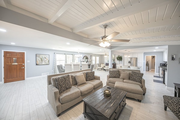 A spacious living room with a high ceiling, a ceiling fan, and a large window.
