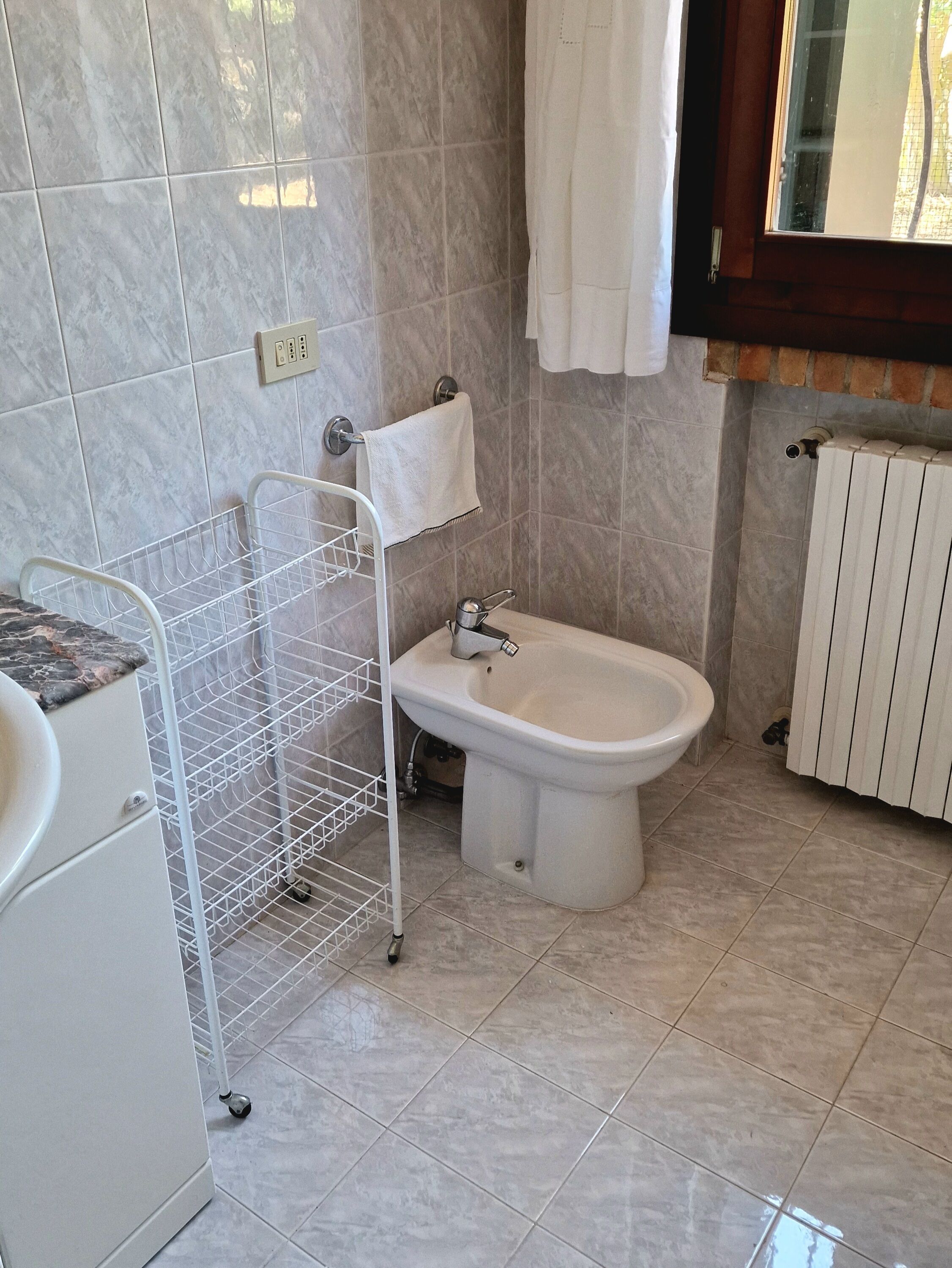 A bathroom with a bidet, a towel rack, a white sink, and a tiled floor.