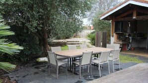 Eine Terrassengruppe im Freien mit Holztisch und Stühlen, umgeben von Grünpflanzen und einem Grillbereich.