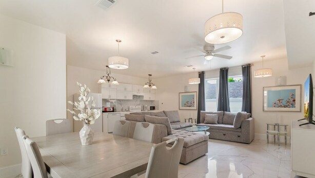 A modern living room with a dining table, sofas, and a kitchen in the background.