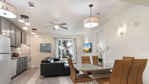 A modern kitchen with stainless steel appliances, a dining area with a glass table and brown chairs, and a ceiling fan.
