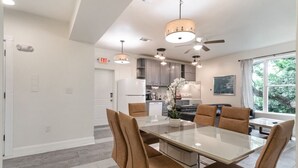 A modern kitchen with grey cabinets, a white refrigerator, and a dining area with a glass table and brown chairs.