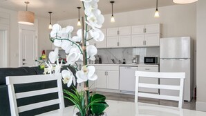 Een moderne keuken met witte kasten, een koelkast en een eethoek met een witte tafel en stoelen.