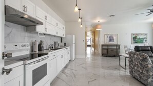 Een moderne keuken met witte kasten, een ingebouwde oven en een magnetron. Er is een eethoek met een tafel en stoelen, en een bank in de woonkamer.