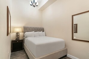 Un dormitorio ordenado con cama, mesita de noche, lámpara y un espejo grande en la pared.