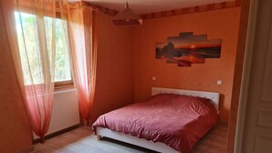 Et soveværelse med seng, radiator, et vindue med let gardin og et billede hængende på væggen.