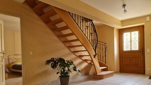 En trappe med trætrin og sorte metalgelændere, der fører op til en etage ovenpå. En potteplante står placeret i nærheden af trappen.