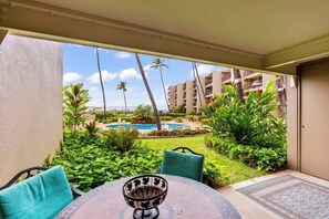 Varanda com mesa e cadeiras, vista para uma piscina e vegetação exuberante.