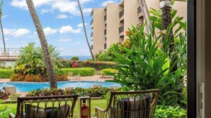 A hotel room with a view of a swimming pool, outdoor seating, and a building in the background.