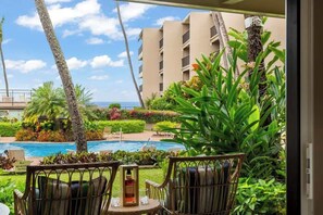 A hotel room with a view of a swimming pool, outdoor seating, and a building in the background.