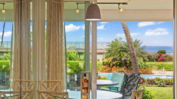 A glass table with chairs, a bottle, and a view of a pool and greenery.