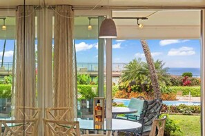 A glass table with chairs, a bottle, and a view of a pool and greenery. - Ground floor, oceanview 1 bedroom condo, steps from amenities, walkable area (Lahaina)