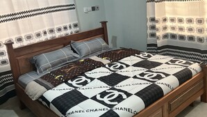 A bedroom with a wooden bed, patterned bedspread, and curtains with geometric designs. - Racapa Apartment (Tema)