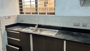 A kitchen with a stainless steel sink, a window with metal bars, and a black countertop. - Racapa Apartment (Tema)