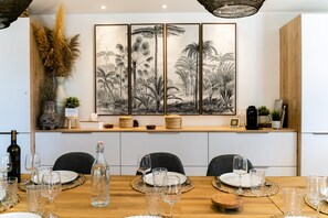 A dining area with a long table set for a meal, a large framed botanical print on the wall, and a variety of decorative items on the sideboard. - Villa Margot, stunning pool, beach 500 m (Agde)