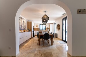 Une cuisine moderne avec un coin repas, comprenant un grand îlot central, des luminaires suspendus et une vue dégagée sur l’extérieur grâce à une arche.