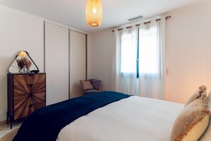 Une chambre à coucher avec un lit, une commode, une chaise et une fenêtre avec des rideaux.