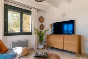 Un salon avec une grande fenêtre, un téléviseur, un meuble en bois, un radiateur, un canapé et une table basse.