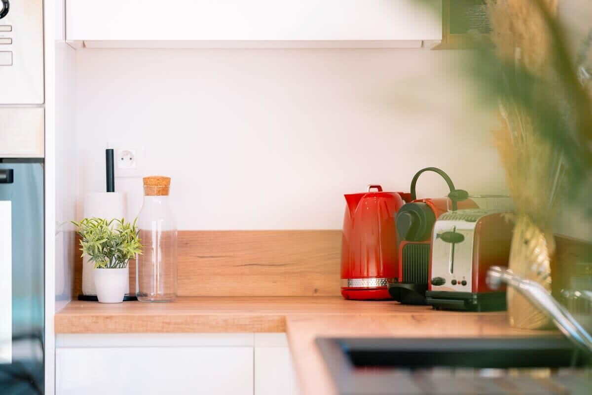 A kitchen counter with a potted plant, a glass bottle, a red kettle, and a green appliance.