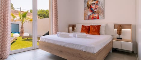 A modern bedroom with a large bed, a painting, and a view of a garden.