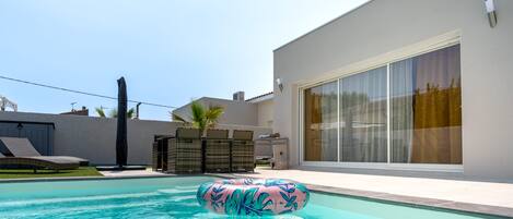 Una piscina con una tumbona y un ventanal grande.