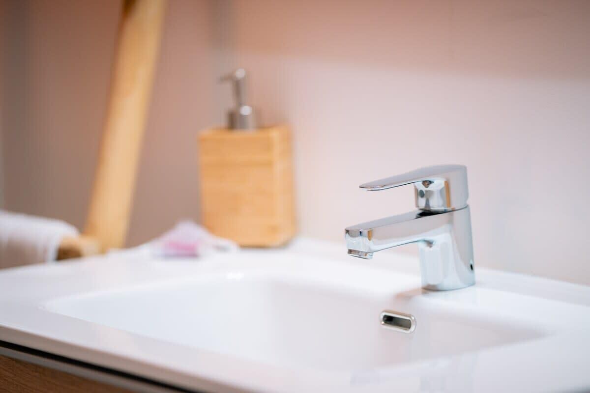 A bathroom sink with a chrome faucet and a soap dispenser in the background.