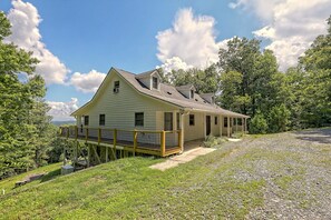 A single-story house with a covered porch and a deck, surrounded by trees and a gravel driveway. - Beautiful long range views at Tranquility Ridge (Blue Ridge)