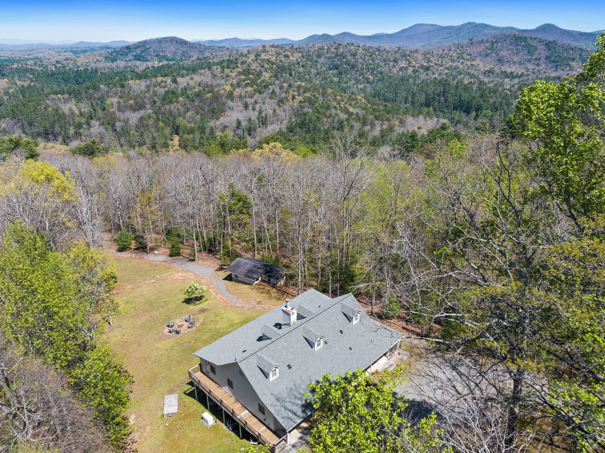 A house with a large deck, surrounded by a forested area with mountains in the background.