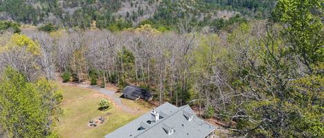 A house with a large deck, surrounded by a forested area with mountains in the background.