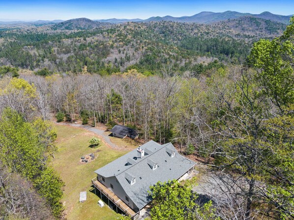 A house with a large deck, surrounded by a forested area with mountains in the background. - Beautiful long range views at Tranquility Ridge (Blue Ridge)