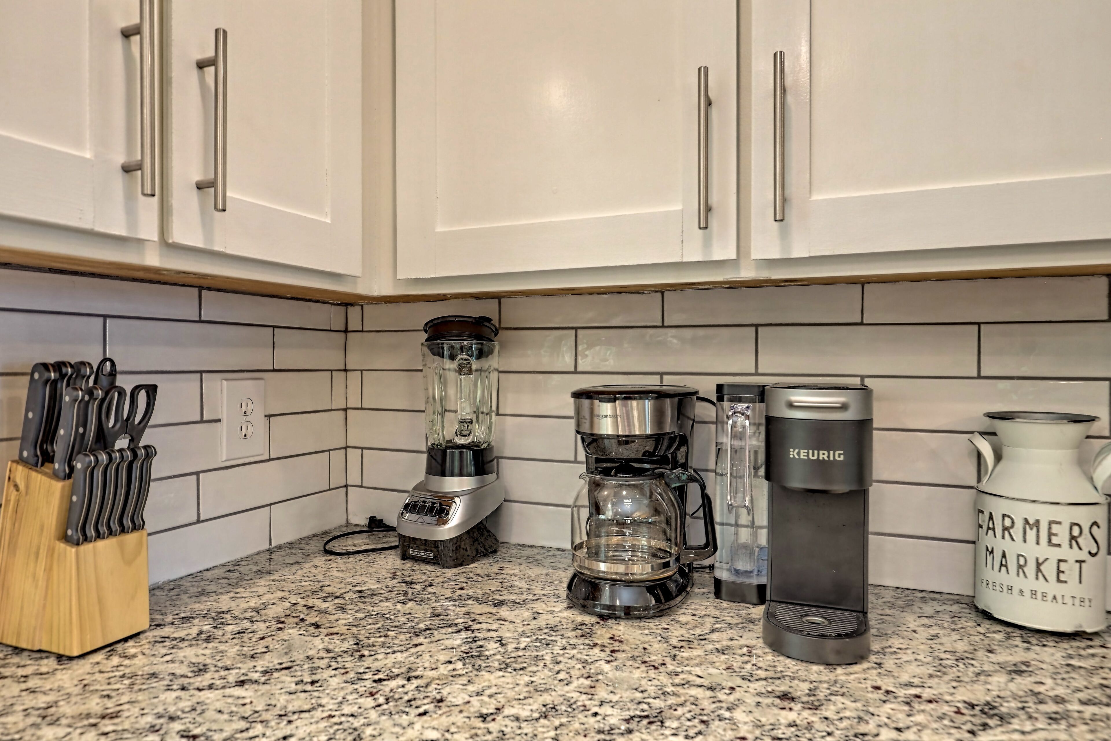 Una cocina con armarios blancos, encimera de granito, licuadora, cafetera y hervidor.
