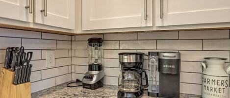 Una cocina con armarios blancos, encimera de granito, licuadora, cafetera y hervidor.