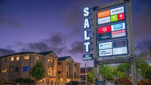 Un edificio con un letrero que dice "SALT DISTRICT" y una pantalla publicitaria digital con diversos anuncios.
