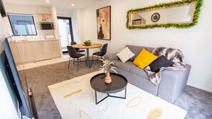 Una sala de estar moderna con un sofá gris, una mesa redonda y un comedor con una mesa pequeña y sillas.