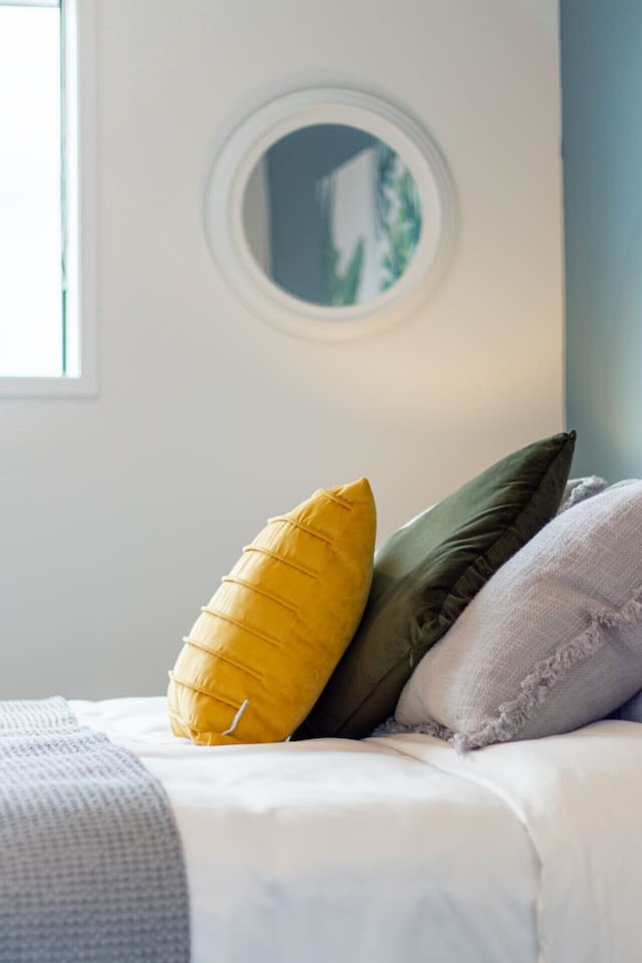 A bed with a white duvet and three pillows in yellow, green, and purple.