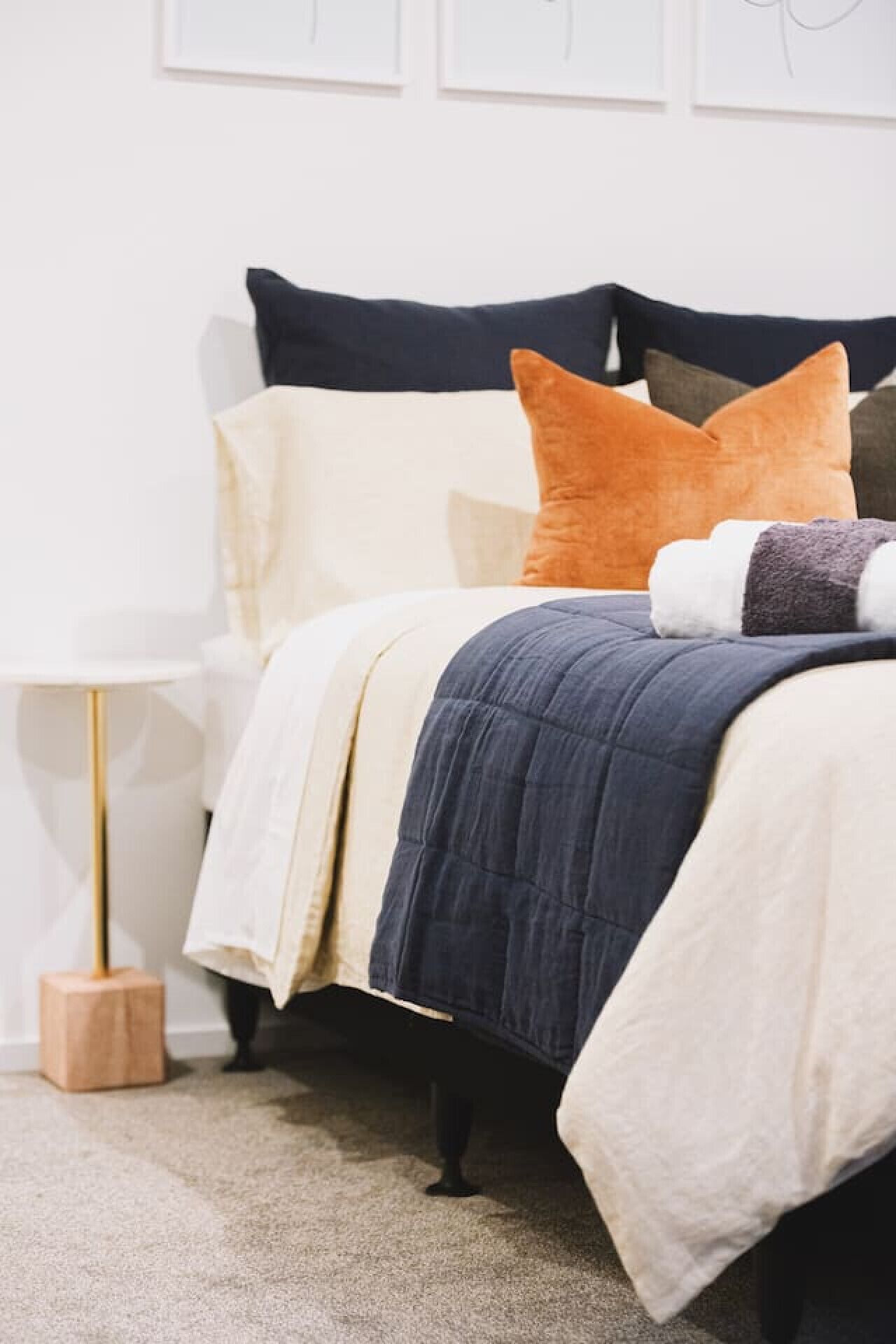 Una cama bien hecha con un edredón azul oscuro, ropa de cama blanca y crema, y una variedad de almohadas.