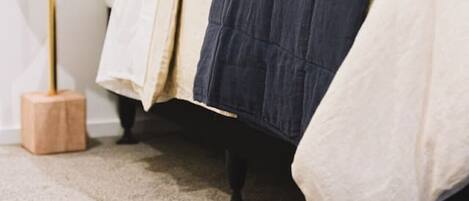 Una cama bien hecha con un edredón azul oscuro, ropa de cama blanca y crema, y una variedad de almohadas.