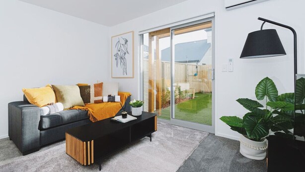 A modern living room with a grey sofa, black coffee table, and a large potted plant. - 1 Bed Central City Fringe Deluxe w/Carpark (Christchurch)