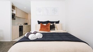 A bedroom with a bed, pillows, a rolled towel, and a wall with three leaf-patterned artworks. - 1 Bed Central City Fringe Deluxe w/Carpark (Christchurch)