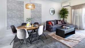 A modern living room with a dining table, grey upholstered chairs, a grey sofa, a black coffee table, and a large plant.