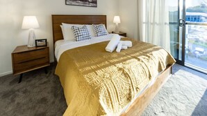 A hotel room with a large bed, two bedside tables, a nightstand, a window with a view, and a framed picture on the wall.
