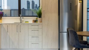 A modern kitchen with light wood cabinetry, a stainless steel refrigerator, and a dining area with a dark chair.