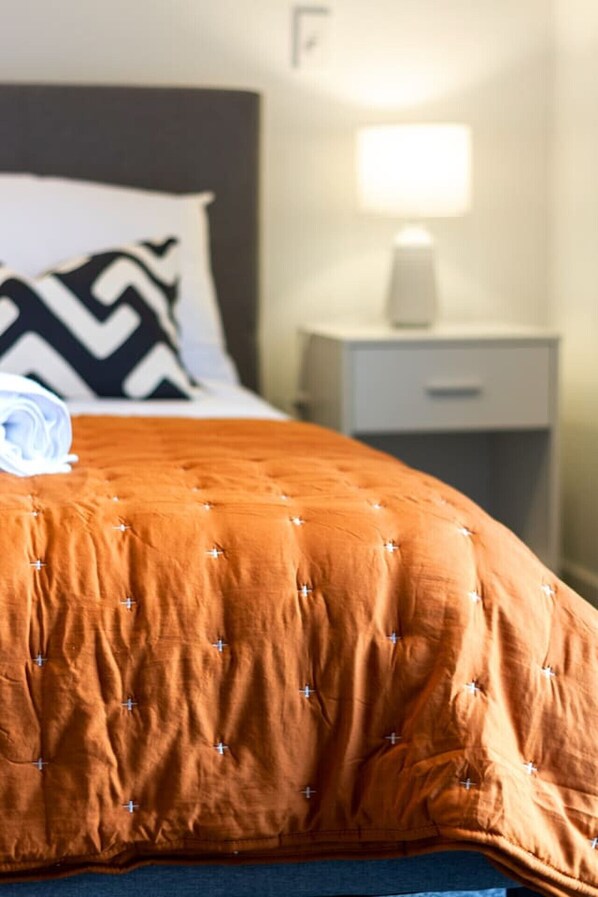 Una cama bien hecha con una colcha naranja y un cojín blanco y negro.