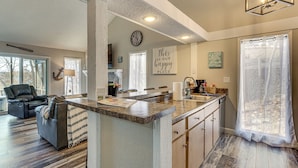 A spacious living area with a large window, a comfortable seating area, and a kitchen with a central island. - Walk to Lake: Osage Beach Home w/ Grill! (Osage Beach)