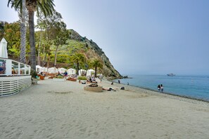 A beach with palm trees, a rocky hillside, and a boat in the water. - Dreamy Catalina Island Home, Walk to Beach & Ferry (Avalon)